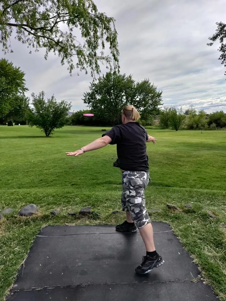 Person mid-throw during a disc golf game in a grassy park—capturing gentle movement for chronic illness through playful, low-impact outdoor activity.