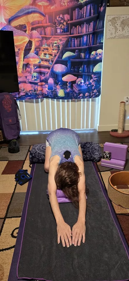 Person in child’s pose on a yoga mat using props for support—demonstrating gentle movement for chronic illness in a cozy, personalized space.