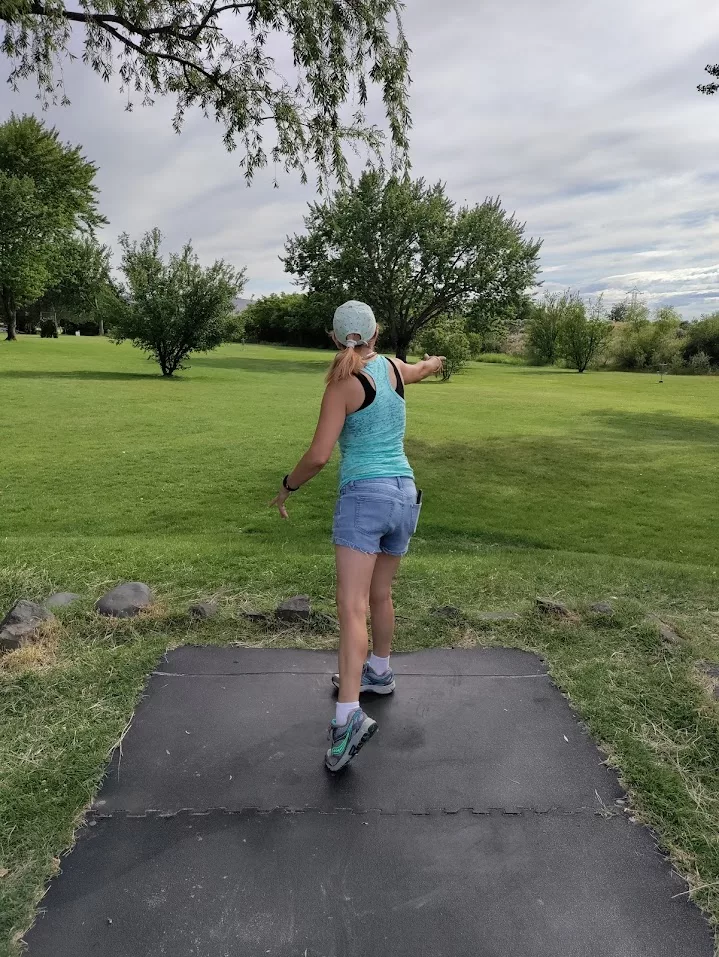 Person throwing a disc on a grassy course under cloudy skies—showcasing gentle movement for chronic illness through low-impact outdoor play.