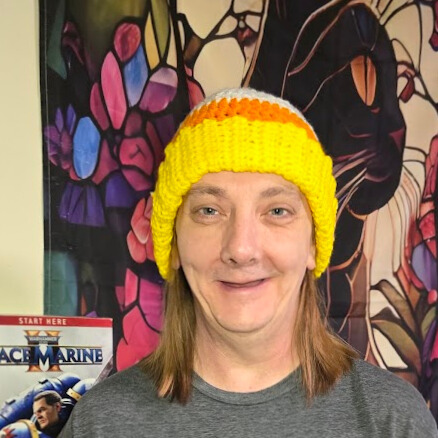 Person wearing a handmade Candy Corn Beanie with bold candy corn stripes, standing in front of a colorful tapestry background.