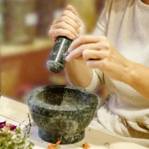 Close up of hands tending a small rosemary plant in a dark ceramic pot, morning light.