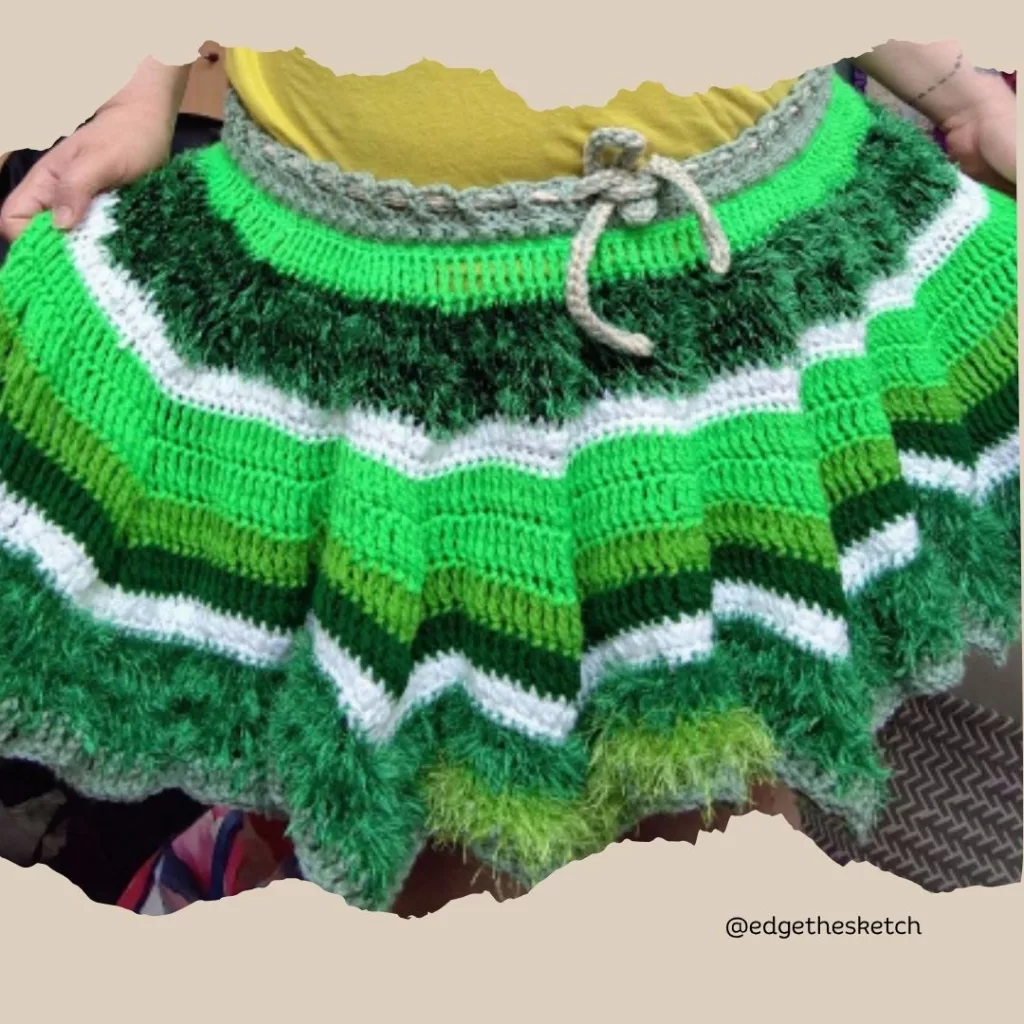 A hand-crocheted skirt featuring the textured Garden Fairy Berry stitch in horizontal stripes of vibrant green, olive green, white, and tan, complete with a matching tied drawstring waistband. From the Garden Fairy Berry Stitch Crochet Skirt Pattern