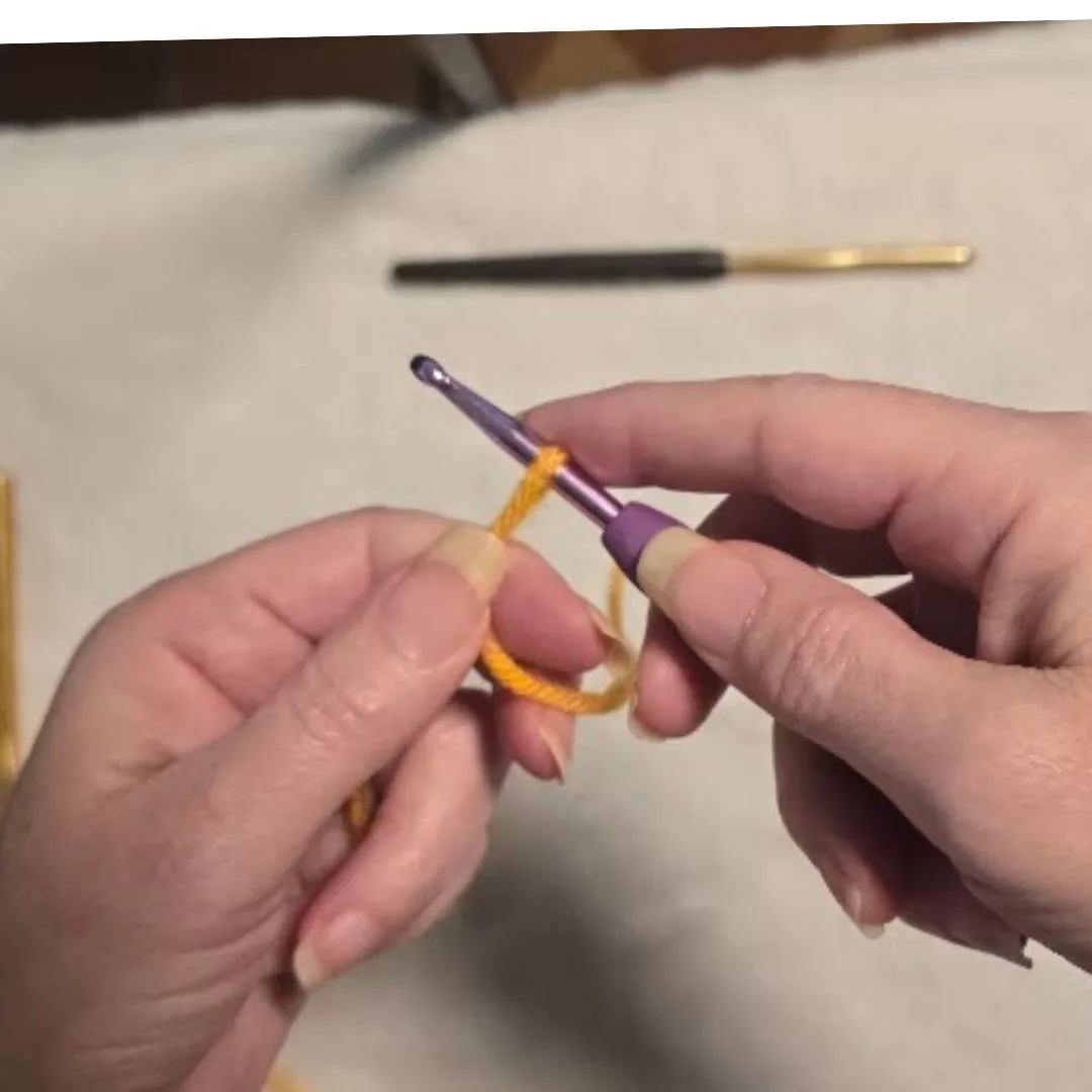 Close-up of the "tighten" step for a slip knot: The person pulls the tail and working yarn in opposite directions, causing the knot to slide up and snug against the blue-handled crochet hook. The resulting loop remains large enough to move freely on the hook's shaft.