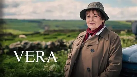 DCI Vera Stanhope wearing her iconic olive green trench coat and bucket hat, standing in a field in Northumberland.