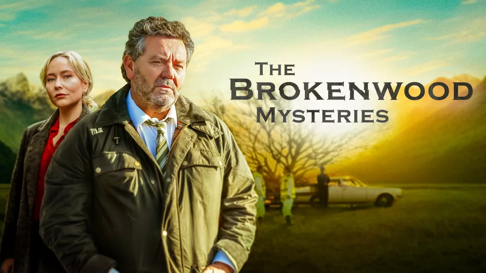 Official series poster for the cozy crime series The Brokenwood Mysteries showing the lead detectives standing outside in front of a vintage car.
