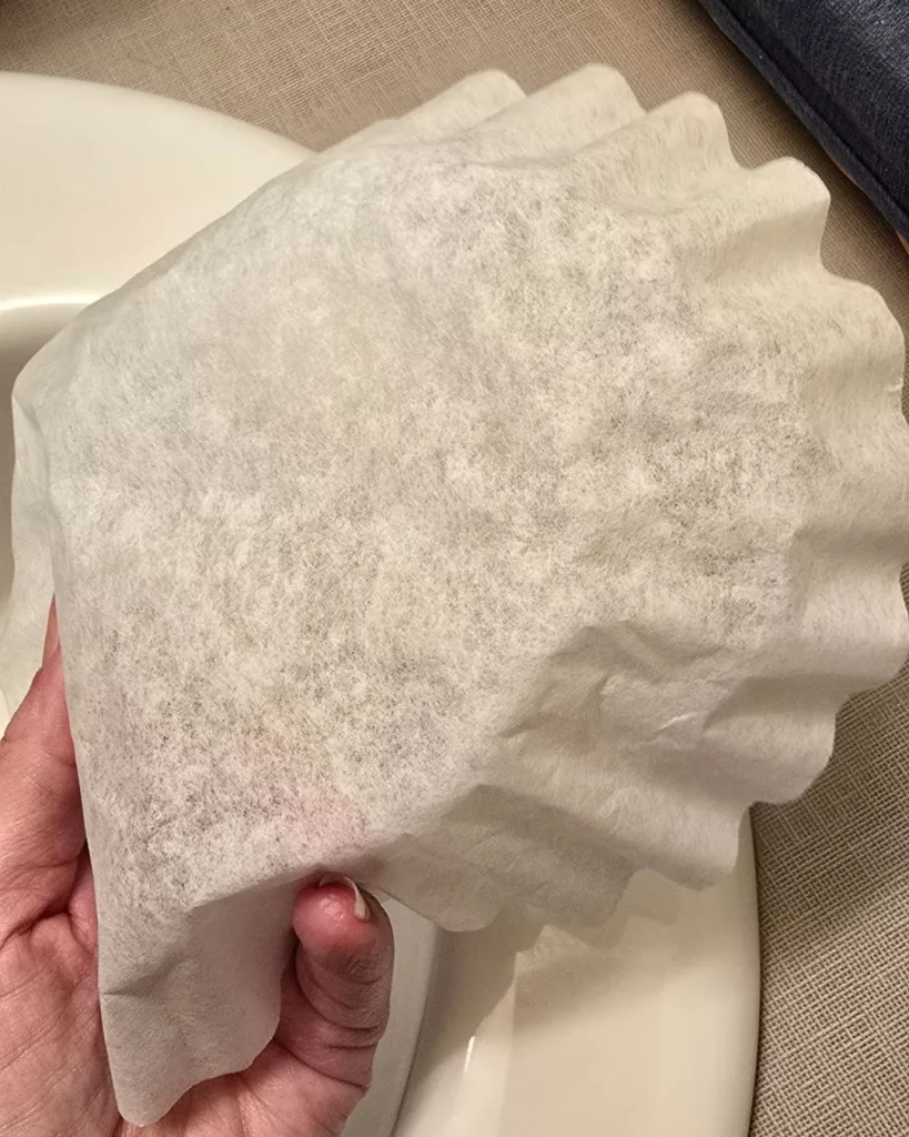 Cleaning a bathroom mirror with a coffee filter, showcasing practical low energy cleaning tips for a streak free shine.
