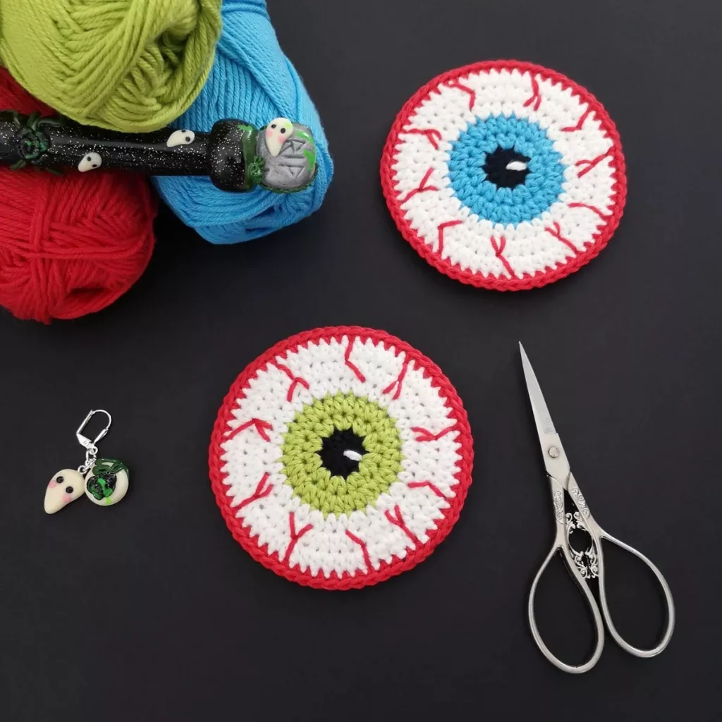 Double-sided crochet eyeball coasters with colorful irises and embroidered bloodshot details.