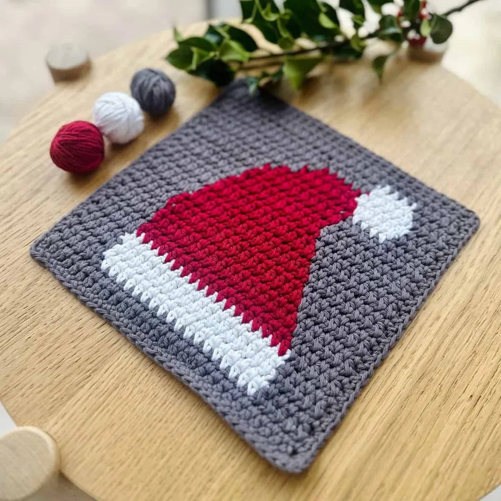 Red and white intarsia crochet Santa hat washcloth lying flat on a wooden counter